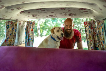 Caucasian young man with his dog, labrador retriever, unpacking minivan. Camping and hiking concept