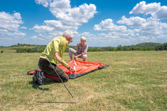 Active senior people setting up the tent in high mountains. Camping and travel concept. - Powered by Adobe