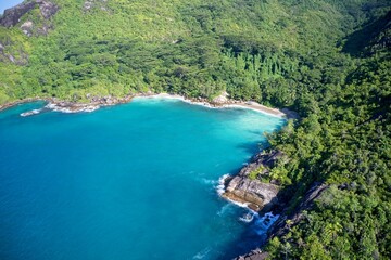 Obraz premium Drone field of view of secret cove with turquoise blue water meeting the forest on secluded island of Mahe, Seychelles.