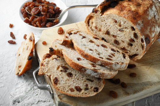 Raisin bread, traditional loaf of sliced bread with cutting board and rustic white plaster background, close-up.