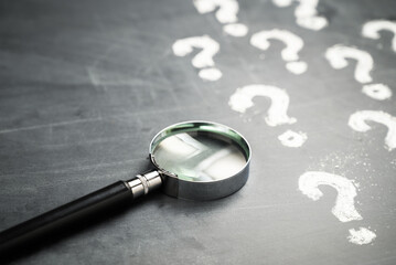 Magnifying glass and many question marks on the blackboard, FAQs, question analysis, education...