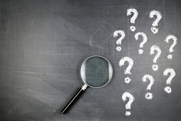 Magnifying glass and many question marks on the blackboard, FAQs, question analysis, education...