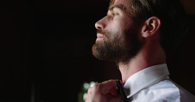 Young bearded man stands at the window and preparing for wedding
