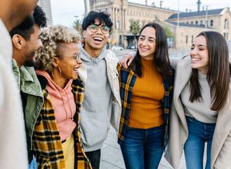 Obraz premium Happy young people laughing together outdoors - Diverse smiling teenager students hugging each other having fun while hanging out in city street