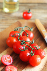 Cherry tomatoes on a branch lie on a wooden board, behind there is oil and a knife lies