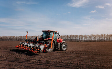 Obraz premium Spring sowing season. Farmer with a tractor sows corn seeds on his field. Planting corn with trailed planter. Farming seeding. The concept of agriculture and agricultural machinery.