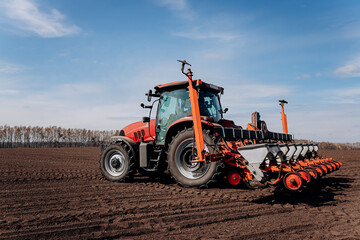 Fototapeta premium Spring sowing season. Farmer with a tractor sows corn seeds on his field. Planting corn with trailed planter. Farming seeding. The concept of agriculture and agricultural machinery.