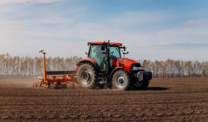 Obraz premium Spring sowing season. Farmer with a tractor sows corn seeds on his field. Planting corn with trailed planter. Farming seeding. The concept of agriculture and agricultural machinery.