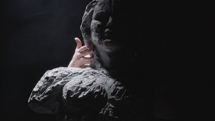 A white statue of a man. Female hands gently touch the statue. A close-up shot on a black...
