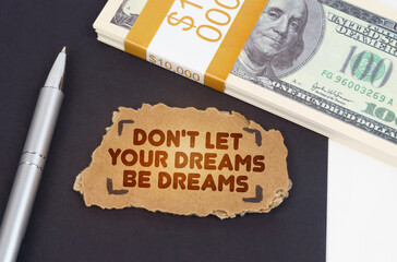 On the table are dollars, a pen and a cardboard sign with the inscription - don t let your dreams be dreams