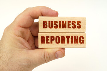 On a white background, a hand that holds wooden blocks with the inscription - Business Reporting