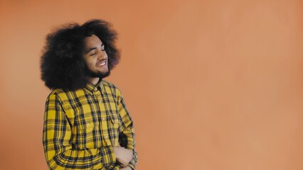 A young man with an African hairstyle on an orange background takes out his phone, looks at the message and puts it back in his pocket. Emotions on a colored background