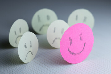 Pink paper smiley face with yellow paper sad faces around it. Concept of being positive in the face...