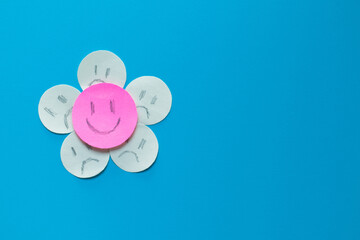 Pink paper smiley face with yellow paper sad faces around it. Concept of being positive in the face of a complicated situation, unique, different.