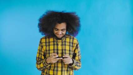 A young man with an African hairstyle on a blue background is playing on the phone. On a colored background