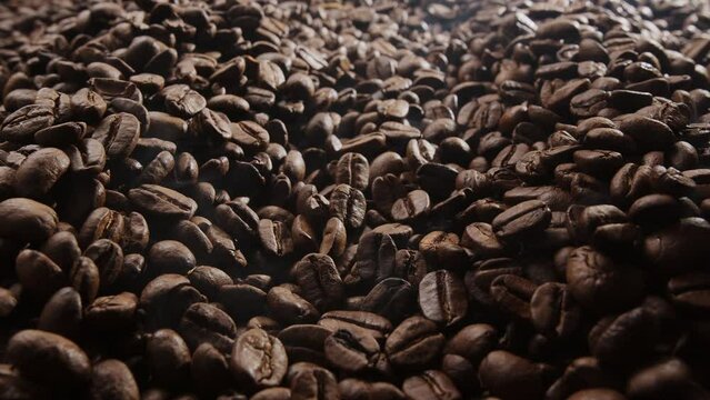 Coffee beans are roasted with little roasted smoke, the camera close up slowly follows the numerous coffee beans. 