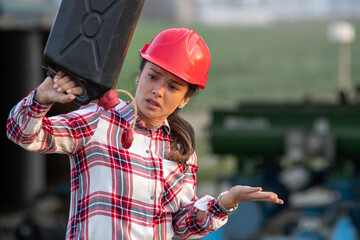 Woman engineer holding an empty jerry can in fornt of industrial plant