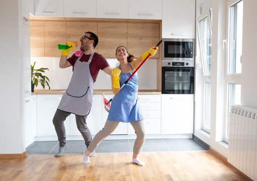 Cheerful couple dancing and singing while cleaning apartment together.