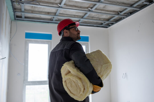 Male worker insulating suspended ceiling with glass wool.