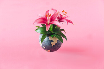 Fresh magenta lillies growing from a globe against pastel pink background. Earth day creative...