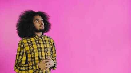 A young man with an African hairstyle on a pink background takes out his phone, looks at the message and puts it back in his pocket. Emotions on a colored background