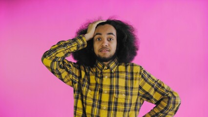 A young man with an African hairstyle on a pink background is surprised. Emotions on a colored...