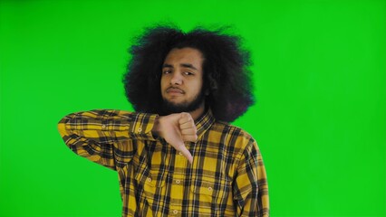 An African-American man looks at the camera, gives a thumbs down, stands isolated on a green background