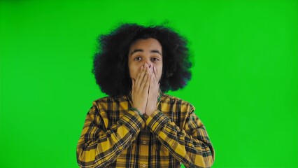 A young man with an African hairstyle on a green background is surprised. Emotions on a colored...