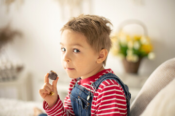 Cute child at home with little newborn chicks, eating chocolate candy in bed