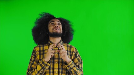 A young man with an African hairstyle on a green background crosses his fingers and prays. Emotions on a colored background.