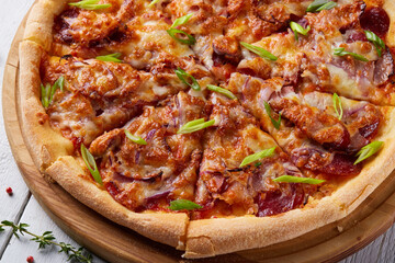 Sliced tasty fresh pizza with cheese, sausage, salami, bacon and red onion. Italian pizza on wood cutting board