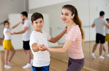 Smiling preteen boy learning dynamic boogie-woogie in pair with his young mother in dance studio...