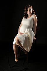 Beautiful pregnant woman in the dress sitting on the chair isolated on the black