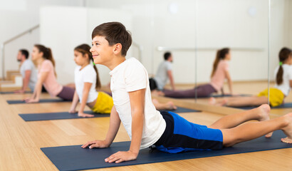 Fototapeta na wymiar Young boy doing cobra pose during family group training in gym.