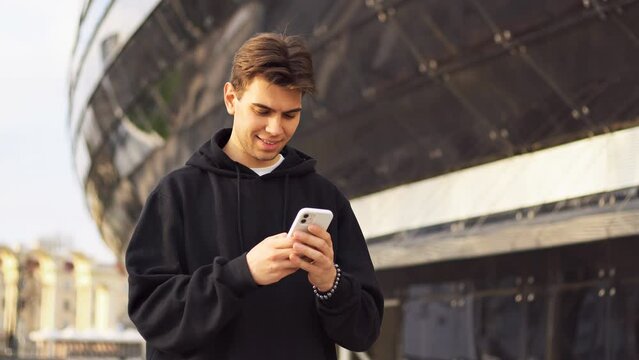 Smiling sports fan holding smartphone and using betting app. Football stadium on the background. Copy space. Gambling concept.