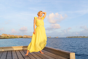 A woman in a yellow dress on the ocean at sunset. - Powered by Adobe