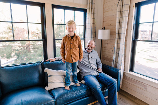 Four Year Old Boy Stands And Smiles On Couch Indoors