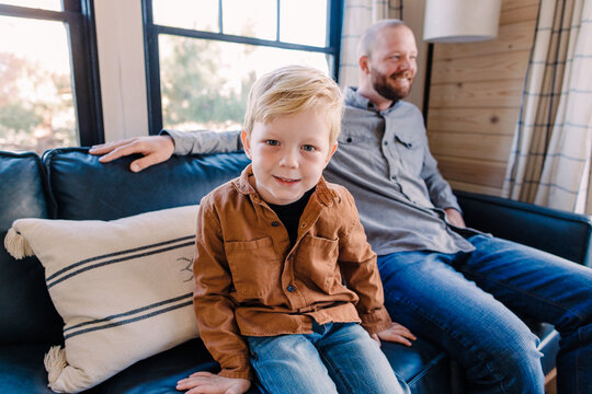 Preschool age Caucasian boy smiles at camera while sitting on couch