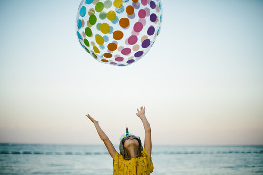 Blond seven year old girl throws rainbow ball by the ocean