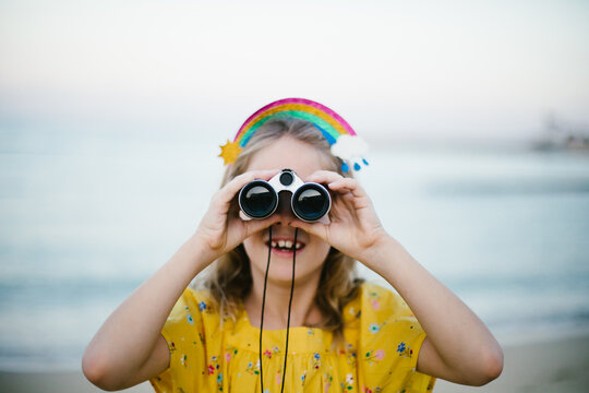 Young blond girl with rainbow headband looking through binoculars