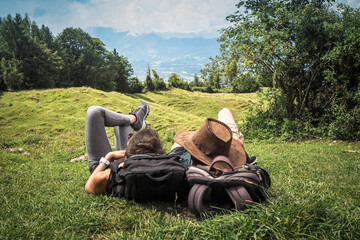 romantic sportive couple lying in the green grass on the mountain top enjoying the view of nature forest after a strenuous hike with their backpacks