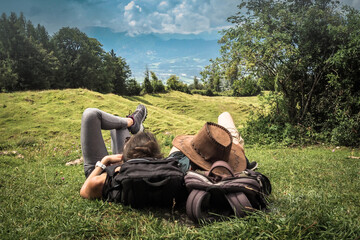 romantic sportive couple lying in the green grass on the mountain top enjoying the view of nature forest after a strenuous hike with their backpacks
