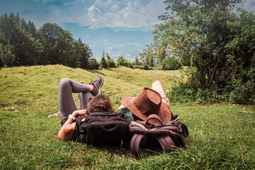 romantic sportive couple lying in the green grass on the mountain top enjoying the view of nature forest after a strenuous hike with their backpacks