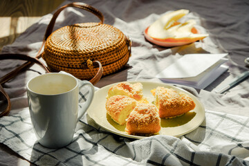 Morning breakfast in bed on blanket with tea, fruit and pie. Wicker bag and notebook. Light green color. Summer mood inspiration.