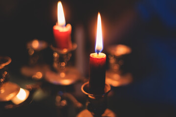 Vintage retro brass candlesticks with red candles burning in a dark room on a black background, cozy night atmosphere with candleholder, candle fire