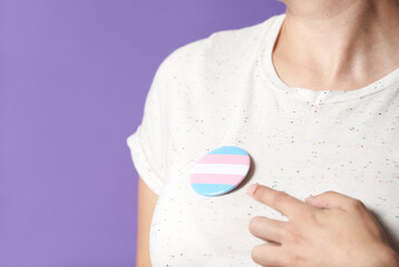Person wearing and pointing a trans flag badge; gender diversity, identity pride - obrazy, fototapety, plakaty