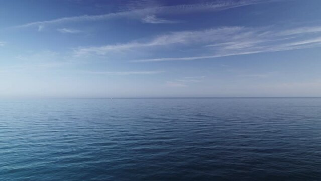 Calm and emtpy blue ocean with scattered clouds, moving backwards