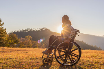 Person sitting on wheelchair looking sunset on mountain park..