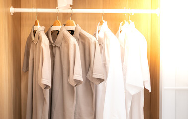 close up collection shade of earth tone color t-shirts hanging ona  wooden clothes hanger in closet or clothing rack.