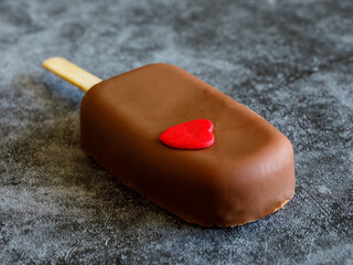 Obraz na płótnie Canvas Chocolate popsicle. ice cream stick with red heart on dark grey marble background. Creative summer food or love valentine day concept. Place for text, copy space, side view close up